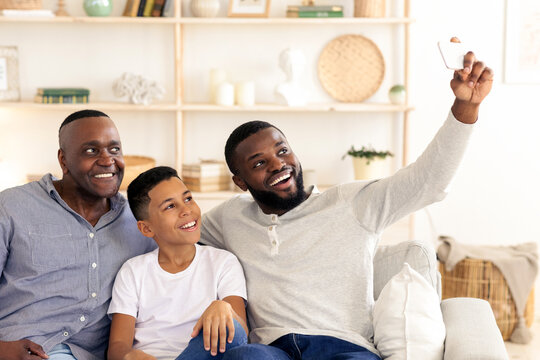 In a cozy living room, a father, son, and uncle share laughter while taking a selfie. The warm atmosphere and smiles highlight their strong family bond during a casual gathering.