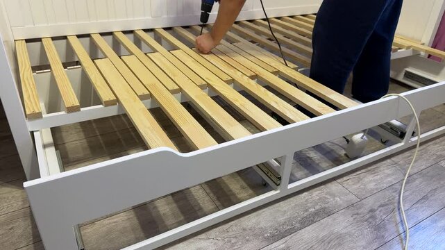 A man assembles a folding sofa bed. He attaches the slats &mdash; lamellas to the base of the couch using a screwdriver.