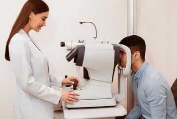 A young man undergoes an eye examination as a professional optometrist operates a testing machine,...