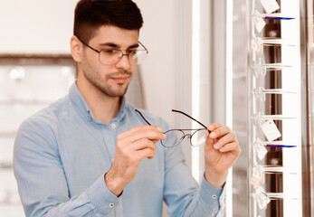 A man is choosing eyeglasses from a display in an eyewear store, carefully examining the frames...