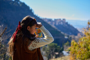 A woman with long dark hair tied with a red ribbon holds tarot cards to her forehead, wearing a...