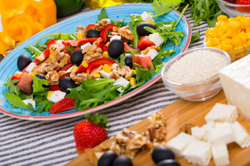 Set of ingredients and ready-made salad with rocket, vegetables and feta cheese on striped background..