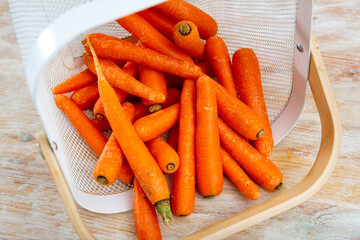 Fresh whole carrots, poured out of a bucket on a wooden table. Close-up image