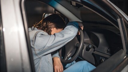 A Young Woman Slumped Over Her Steering Wheel, Exhausted And Overwhelmed In Her Car At Night, Dark...