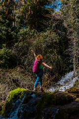 Obraz premium Female hiker celebrating on mossy rocks near waterfall in lush forest