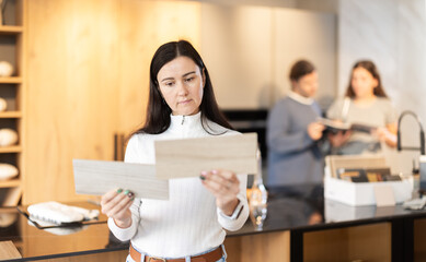 Adult focused woman chooses wood for kitchen decoration in a furniture salon. Customer of a store in the renovation department is looking at wooden samples for the floor and laminate flooring