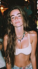 Young woman with long wavy brown hair wearing a white sleeveless top and layered necklace