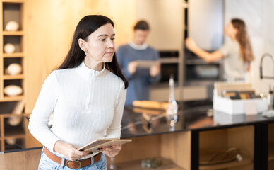 Adult focused woman chooses wood for kitchen decoration in a furniture salon. Customer of a store in the renovation department is looking at wooden samples for the floor and laminate flooring