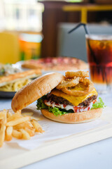 A delicious cheeseburger with lettuce, tomato and melted cheese, served with crispy fries, onion rings and fresh salad. Blurry iced tea is visible behind it