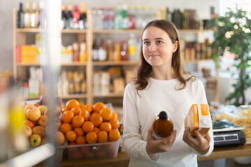 Teenage girl buyer chooses natural peach and tomato juices in grocery store