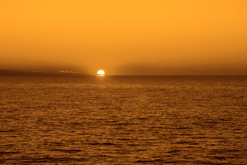 sunset at Black sea, big red disk of sun move down. sun above horizon line. Sun setting above the ocean water. Orange sky at golden hour. perspective view. Cloudy skyline