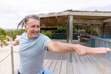 Fototapeta premium Smiling man practicing yoga on wooden deck at beachside retreat, copy space