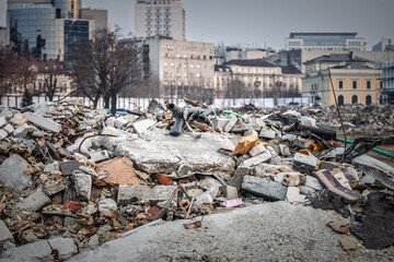 Pile of construction debris including concrete, bricks, and twisted metal from a demolished building, with cityscape of Belgrade in the background.
