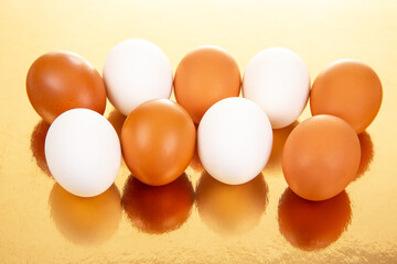 A row of white and brown eggs arranged neatly on a reflective golden surface, showcasing a warm and glossy food photography composition with soft shadows.