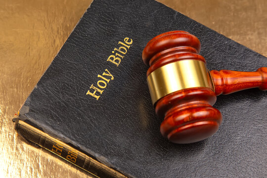Detailed image of a courtroom gavel resting on a "Holy Bible" with embossed gold text, set against a reflective gold background, merging justice and religion.