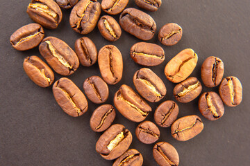 Detailed view of roasted coffee beans, highlighting their warm brown shades and natural fissures on a dark background. Suitable for caffeine-related projects.