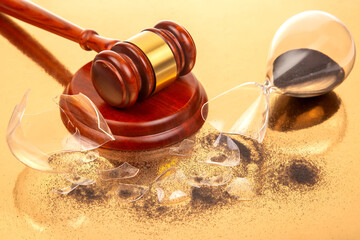 A finely crafted wooden gavel stands beside a fractured hourglass with black sand, photographed on...