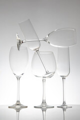 A sleek row of five wine glasses with slender stems, their reflections creating a striking effect on a glossy table, ideal for modern dining or wine aesthetics.