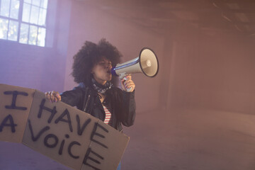 Person holding megaphone and sign, passionately advocating in spacious warehouse, copy space