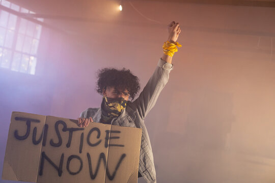 Person holding protest sign, raising fist, advocating for justice in warehouse, copy space