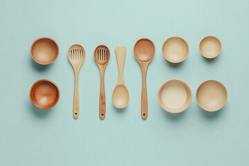 Different wooden kitchen utensils arranged neatly on a blue background with bowls and spoons displayed harmoniously
