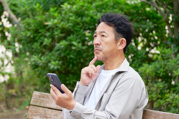 Fototapeta premium スマートフォンを使う中年の男性 考える 屋外