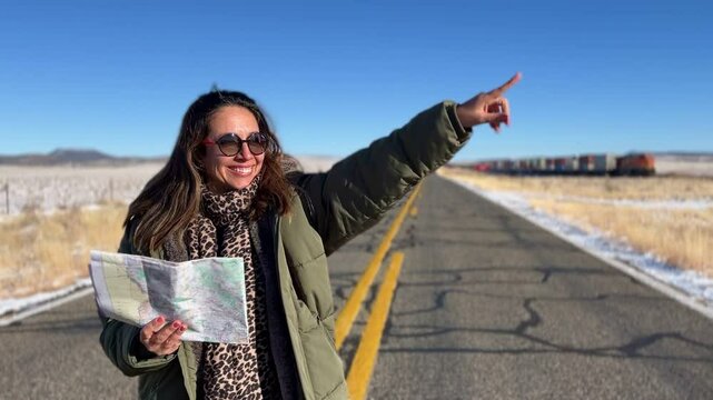 Experienced tourist navigating Route 66 highway, holding map and pointing direction, with freight train passing across snowy winter landscape in background