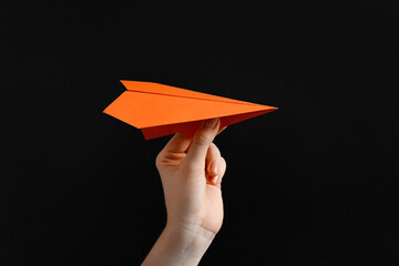 Woman with orange paper plane on black background, closeup