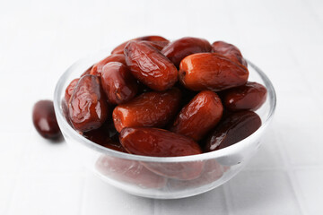 Tasty dried dates in glass bowl on white tiled table, closeup