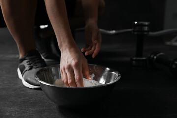 Woman applying talcum powder onto her hands above bowl before training in gym, closeup