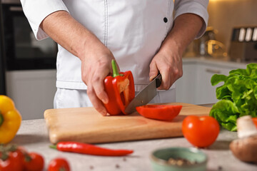 Professional chef cutting bell pepper at table in kitchen, closeup