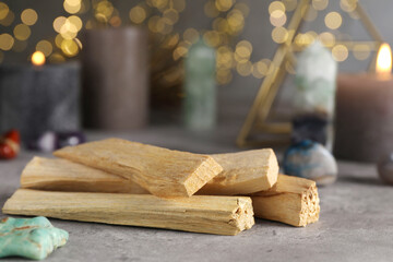 Palo santo sticks and gemstones on grey table against blurred lights, closeup