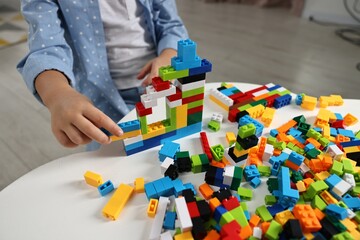 Girl playing with building blocks at white table indoors, closeup