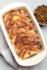 Delicious bread pudding in baking dish and raisins on light gray table, flat lay