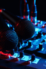 Professional mixing console with microphones on black background in neon lights, closeup