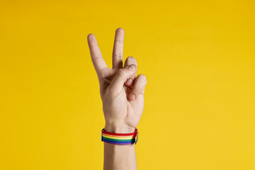 Man with bracelet in colors of LGBT flag showing peace sign on yellow background, closeup