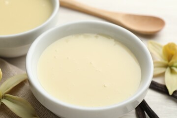 Tasty condensed milk, vanilla pods, flowers and spoon on white table, closeup
