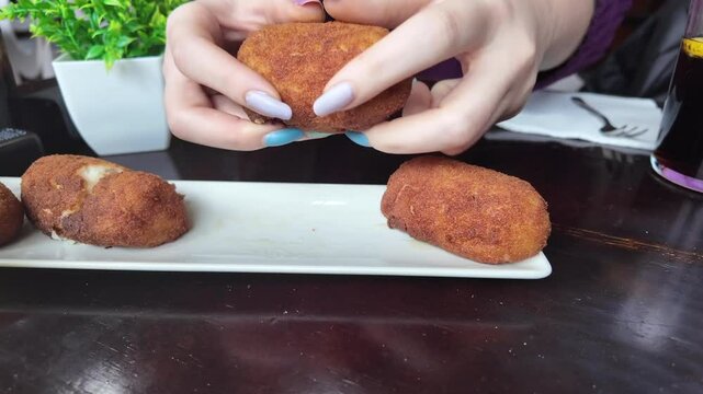 closeup view of the hand of a young white woman picking up a Spanish traditional croquette to eat it.