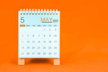 May 2025 desk calendar stand on orange textile background.