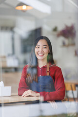 Opening small business. Happy asian woman in apron near bar counter holding digital tablet and looking at camera, waiting for clients in modern loft cafe
