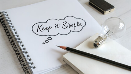 A composition featuring the phrase 'Keep it Simple' in a notebook alongside a lightbulb, set against a clean, white background.