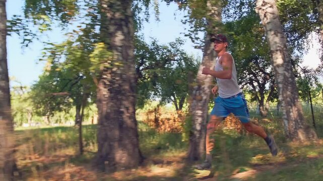 A young runner in a tank top sprints through a birch grove, training endurance and speed for trail running competitions, overcoming obstacles and improving his results for upcoming challenges.