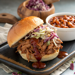 Delicious pulled pork sandwich with coleslaw and a side of baked beans, perfect for a satisfying meal on a dark wooden tray.