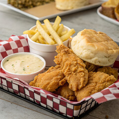 Delicious fried chicken tenders served in a basket with french fries, biscuit, and dipping sauce for a tasty and satisfying meal.