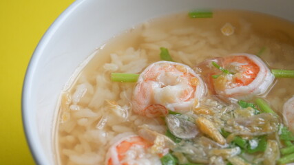 rice soup with shrimp in white bowl on yellow background