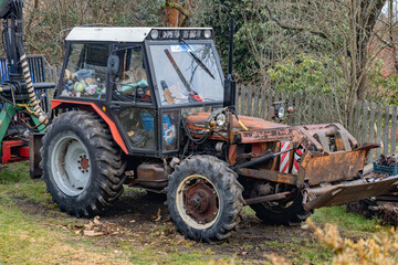 A tractor with a cabin full of junk stands in the yard of a family farm