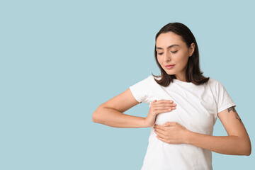 Young woman checking her breast on blue background. Cancer awareness concept
