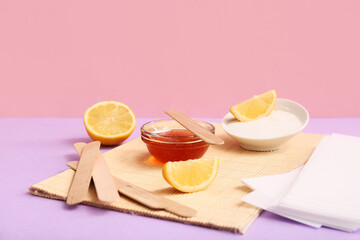 GLass bowl with sugaring paste, wax strips, wooden sticks and lemon on colorful background