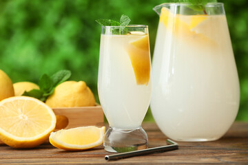Glass and jug of fresh lemonade with mint on wooden table outdoors
