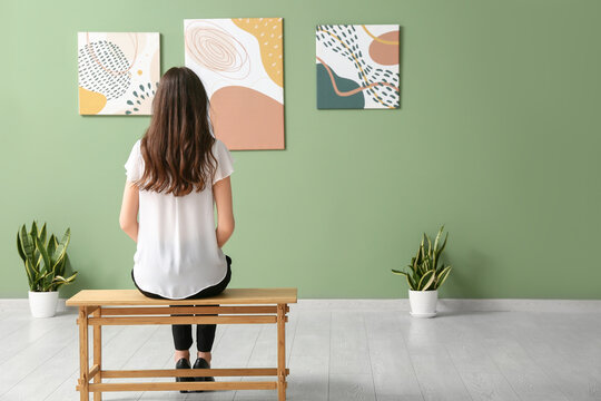 Young woman sitting on bench near paintings in art gallery, back view